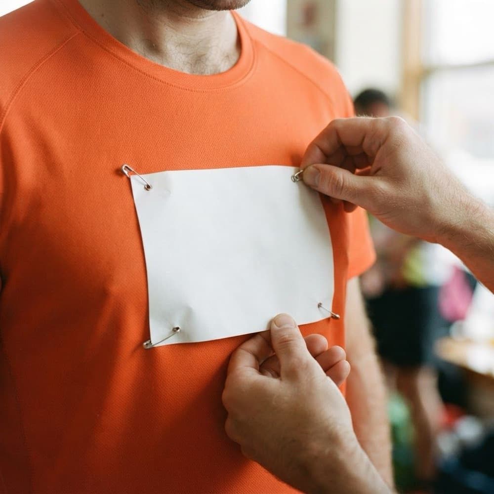 Handen spelden een leeg startnummer op een hardloopshirt